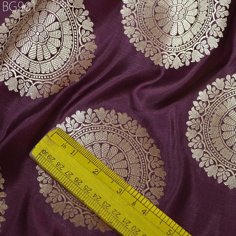 May include: Purple fabric with a repeating pattern of gold circular designs. A yellow ruler is placed on the fabric to show the scale of the design. The ruler measures 4 inches.