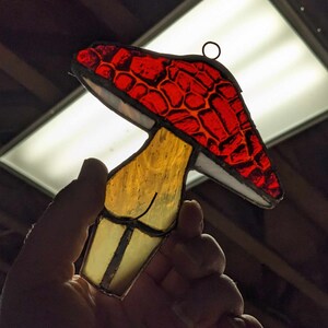 May include: A stained glass mushroom ornament with a red and orange cap and a yellow stem.