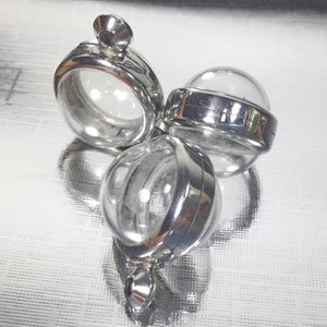 Op de afbeelding: Drie zilveren hanger met transparante glazen inzetstukken. De hangers zijn rond en hebben een scharnieropening.