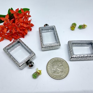 May include: Three silver-toned pendant frames with clear glass inserts. The frames have an ornate design and are perfect for holding small charms or other trinkets.