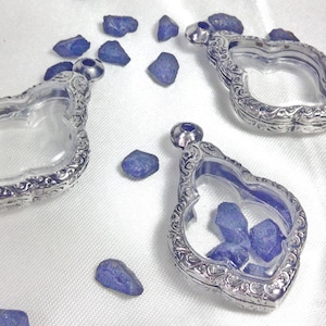 May include: Three silver locket pendants with ornate designs. Each locket has a clear glass insert and is open to reveal a small amount of blue stones inside.