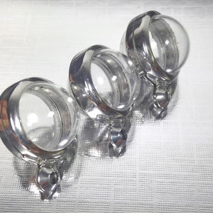 May include: Three silver-toned metal charms with clear glass round containers. Each charm has a hinged lid and a loop for attaching to a necklace or bracelet.