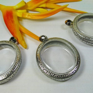 May include: Three silver oval-shaped locket pendants with clear glass inserts. The lockets have a decorative border and are ready to be filled with a special memory.