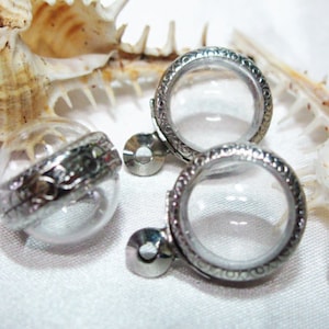 May include: Two silver-toned locket pendants with clear glass inserts. The lockets have a decorative etched design around the edge.