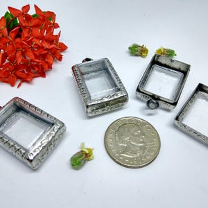 May include: Four silver-toned metal frames with clear glass inserts. The frames are rectangular and have a decorative design. They are arranged on a white surface.