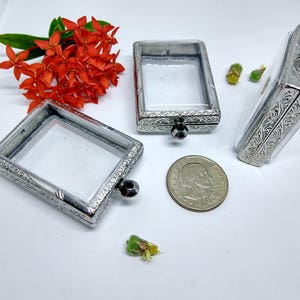 Puede incluir: Tres vitrinas cuadradas de cristal transparente adornadas con plata, con tapa con bisagras y un pequeño lazo en la parte superior. Las vitrinas están sobre una superficie blanca.