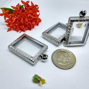 May include: Three silver-toned pendant frames with clear glass inserts. The frames have an ornate design and are perfect for holding small charms or other trinkets.