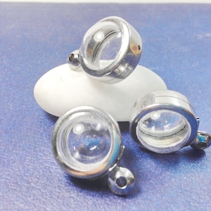 May include: Three silver-toned metal round pendant charms with clear glass inserts. The charms have a loop at the top for attaching to a necklace or bracelet.