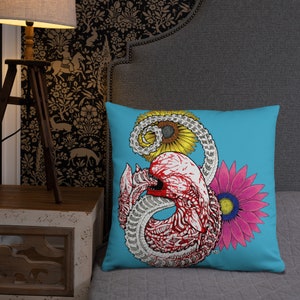 May include: A blue cushion featuring a graphic of a red and white alien creature surrounded by yellow sunflowers and a pink flower.