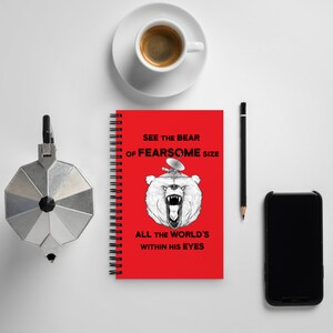 May include: Red spiral bound notebook with a black and white illustration of a bear with a satellite dish on its head. The text on the notebook reads "See the bear of fearsome size all the world's within his eyes."