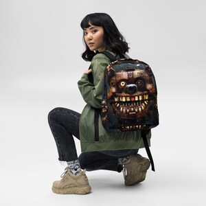 Könnte beinhalten: Ein schwarzer Rucksack mit einem Motiv eines Roboterbären mit einem bedrohlichen Grinsen. Der Bär hat ein metallisches, rostiges Aussehen und trägt einen schwarzen Hut. Der Rucksack hat verstellbare Träger und einen Reißverschluss.