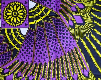 May include: Close-up of a vibrant fabric with a repeating pattern. The design features a central square with a yellow floral motif, surrounded by purple, yellow, and black geometric shapes, resembling feathers or wings.