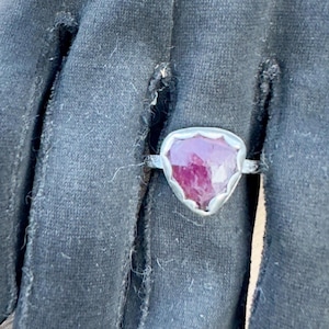May include: A silver ring with a triangular shaped ruby gemstone. The ruby is a deep red color and has a faceted cut.