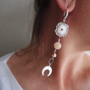 May include: Silver-toned dangle earring featuring a white and gray agate stone, peach-colored beads, and a white crescent moon charm. The earring is suspended from a lever-back closure. The design incorporates natural elements and a celestial theme.