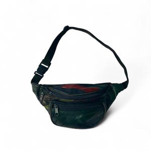 Puede incluir: Riñonera de cuero negro con una correa y hebilla negras ajustables. La riñonera tiene un bolsillo frontal con cremallera y un compartimento principal con cremallera. La parte superior de la riñonera tiene detalles en rojo y verde.