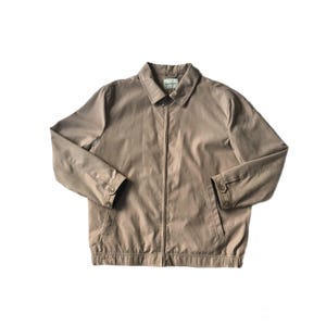 May include: A tan-colored jacket with a full-length zipper, buttoned cuffs, and a collared neckline. The jacket has a simple, classic design, suitable for various occasions. The jacket is made of a smooth, possibly cotton or synthetic material.