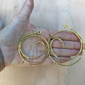 May include: A pair of gold-toned hoop earrings with a spiral design. The earrings are made of hammered metal and have a slightly textured finish.