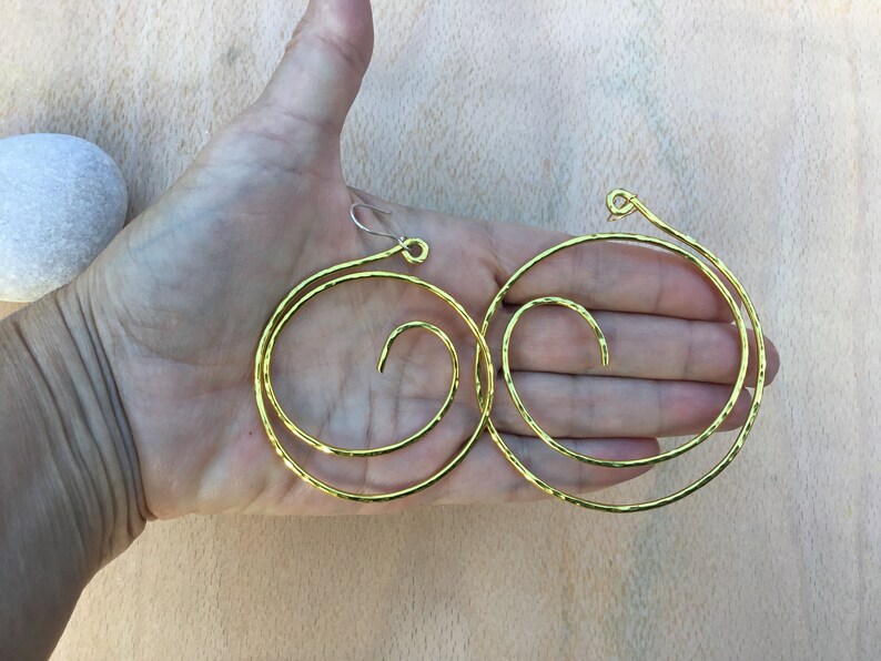 May include: A pair of gold-toned hoop earrings with a spiral design. The earrings are made of hammered metal and have a slightly textured finish.