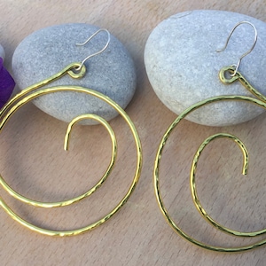 May include: A pair of gold-toned hammered metal earrings with a spiral design. The earrings are large and circular, with a hook closure.