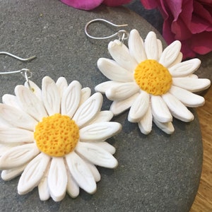 May include: A pair of white daisy earrings with yellow centres. The earrings are made of polymer clay and have silver hooks.