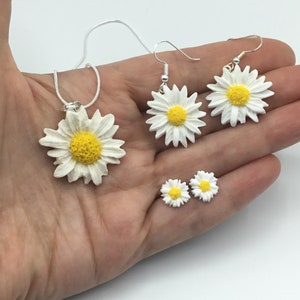 May include: A set of daisy flower jewelry, including a necklace, dangle earrings, and stud earrings. The flowers are white with yellow centers.