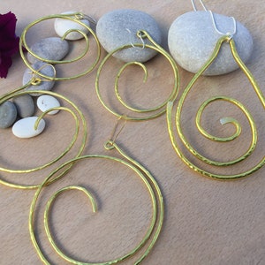 May include: A set of three gold-toned earrings and a necklace featuring a spiral design. The earrings are hoop-shaped and the necklace is a teardrop shape.