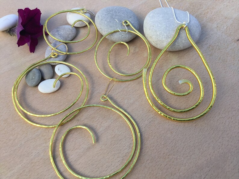 May include: A set of three gold-toned earrings and a necklace featuring a spiral design. The earrings are hoop-shaped and the necklace is a teardrop shape.