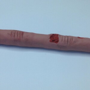 May include: A realistic-looking finger pen with red blood splatter details. The pen is made of a soft, fleshy material and has a black ink tip.