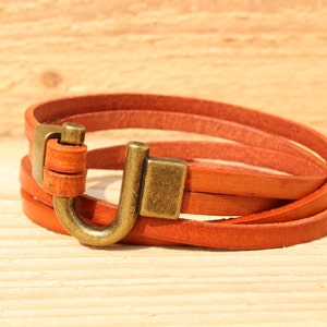 May include: A brown leather bracelet with a metal hook clasp. The bracelet is made of three strands of leather and has a simple, minimalist design.