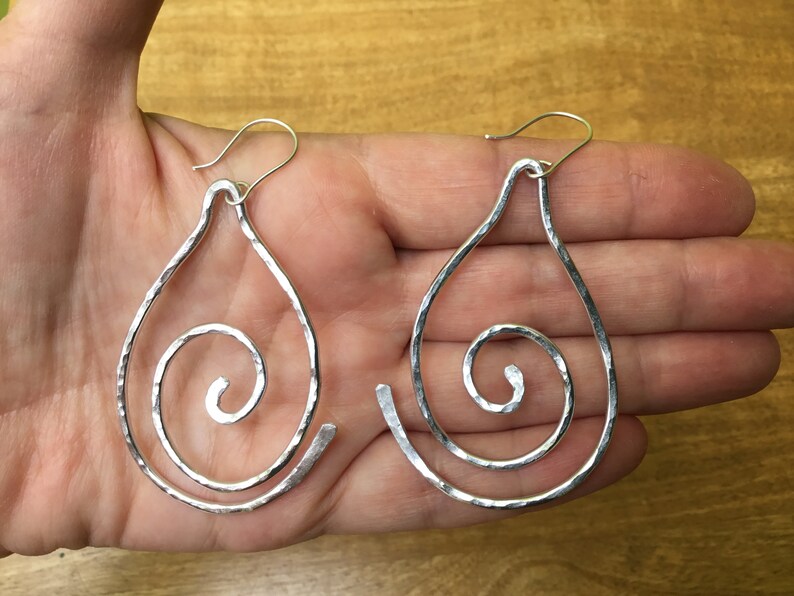 May include: A pair of silver teardrop-shaped earrings with a hammered texture and a spiral design.