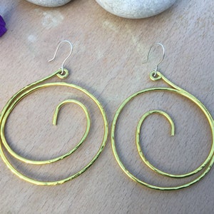 May include: A pair of gold-toned hoop earrings with a spiral design. The earrings are made of hammered metal and have a simple hook closure.