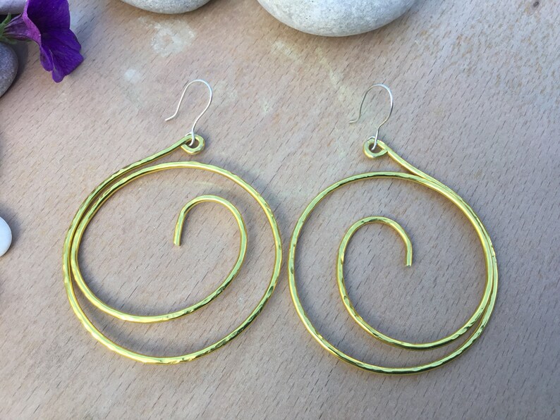May include: A pair of gold-toned hoop earrings with a spiral design. The earrings are made of hammered metal and have a simple hook closure.