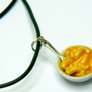 May include: A black cord necklace with a silver spoon and a small white bowl filled with yellow macaroni cheese.