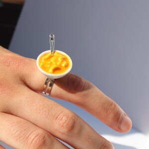 May include: A ring featuring a miniature bowl of macaroni cheese, complete with a tiny spoon.