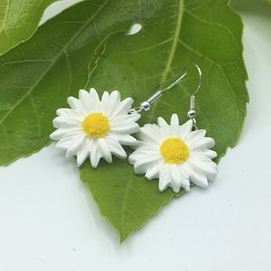 May include: A pair of white daisy earrings with yellow centres. The earrings are hanging from silver hooks.