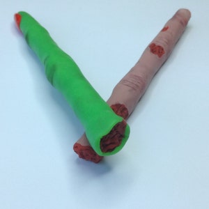 May include: Two fake fingers made of playdough. One finger is green and the other is flesh-colored with red painted details.