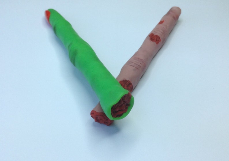 May include: Two fake fingers made of playdough. One finger is green and the other is flesh-colored with red painted details.