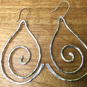 May include: A pair of silver teardrop-shaped earrings with a hammered finish. Each earring features a spiral design.