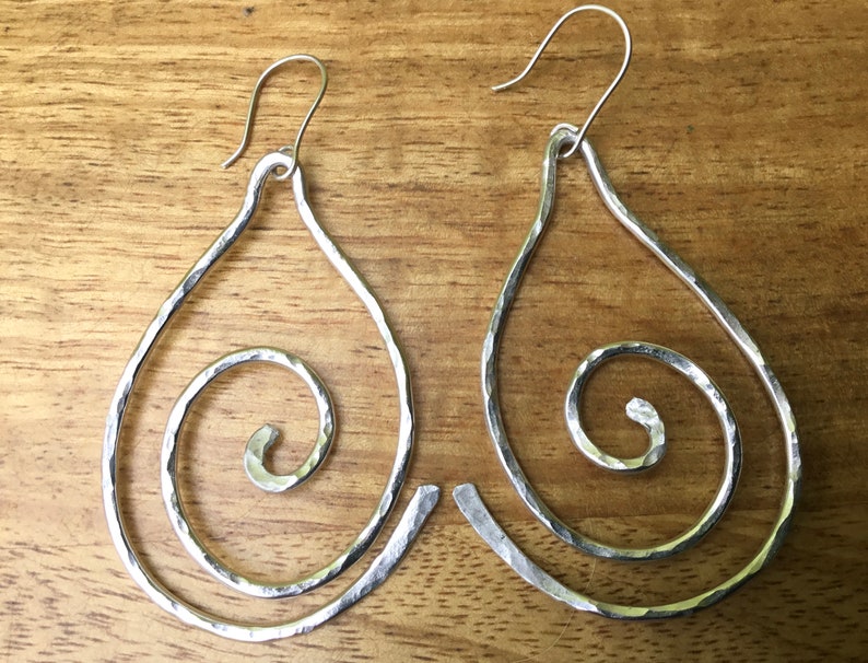 May include: A pair of silver teardrop-shaped earrings with a hammered finish. Each earring features a spiral design.