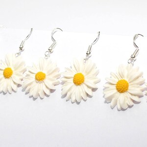 May include: Five pairs of white daisy earrings with yellow centres. The earrings are made of polymer clay and have silver hooks.