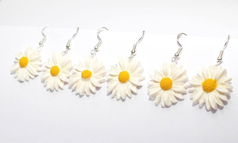 May include: Five pairs of white daisy earrings with yellow centres. The earrings are made of polymer clay and have silver hooks.