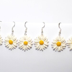 May include: Six pairs of silver dangle earrings with white daisy flower charms. The daisies have yellow centers.