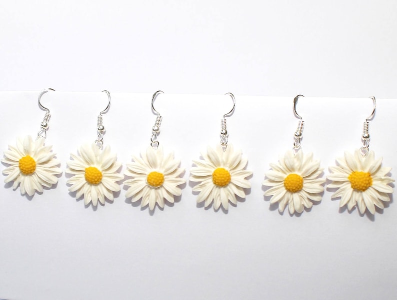 May include: Six pairs of silver dangle earrings with white daisy flower charms. The daisies have yellow centers.