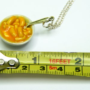 Puede incluir: Un collar de cadena de plata con un taz&oacute;n de cer&aacute;mica en miniatura de macarrones con queso. El taz&oacute;n tiene aproximadamente 2,5 cm de di&aacute;metro y tiene una peque&ntilde;a cuchara unida al lado. El collar mide 4,88 metros de largo.