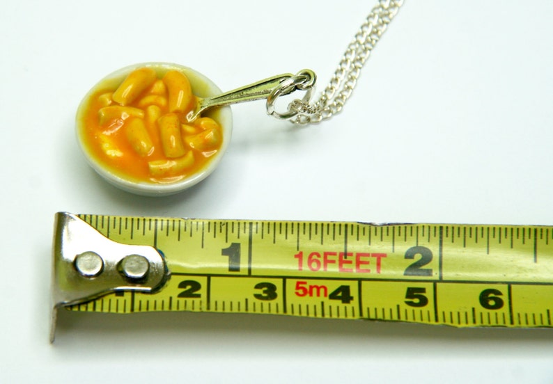 Puede incluir: Un collar de cadena de plata con un taz&oacute;n de cer&aacute;mica en miniatura de macarrones con queso. El taz&oacute;n tiene aproximadamente 2,5 cm de di&aacute;metro y tiene una peque&ntilde;a cuchara unida al lado. El collar mide 4,88 metros de largo.