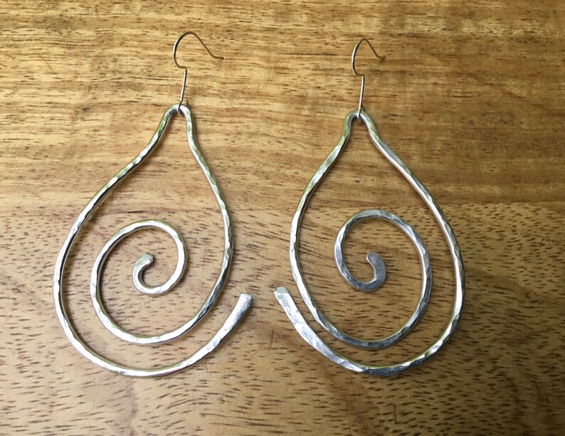 May include: A pair of silver teardrop-shaped earrings with a hammered texture and a spiral design.