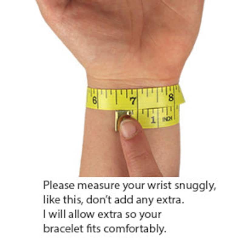 May include: A person's wrist is being measured with a yellow measuring tape. The tape shows measurements in inches, with the wrist measuring approximately 7 inches. Text on the image advises measuring the wrist snugly.