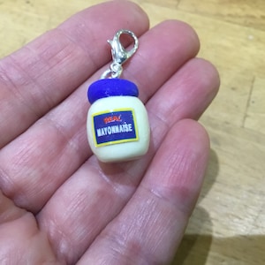 May include: A silver charm shaped like a mayonnaise jar with a blue lid and the words "REAL MAYONNAISE" on the label.