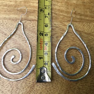 May include: A pair of silver teardrop-shaped earrings with a spiral design. The earrings are approximately 2 inches long.