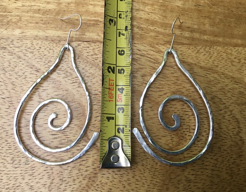 May include: A pair of silver teardrop-shaped earrings with a spiral design. The earrings are approximately 2 inches long.